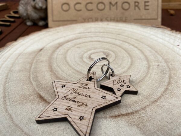 Two oak star keyrings engraved with “This [Mummy/Auntie/Nanny/Granny/Grandpa/Grandad] belongs to” on the large star and a name on the smaller make a charming personalised gift. Shown on wood with a blurred Occomore Yorkshire sign behind.
