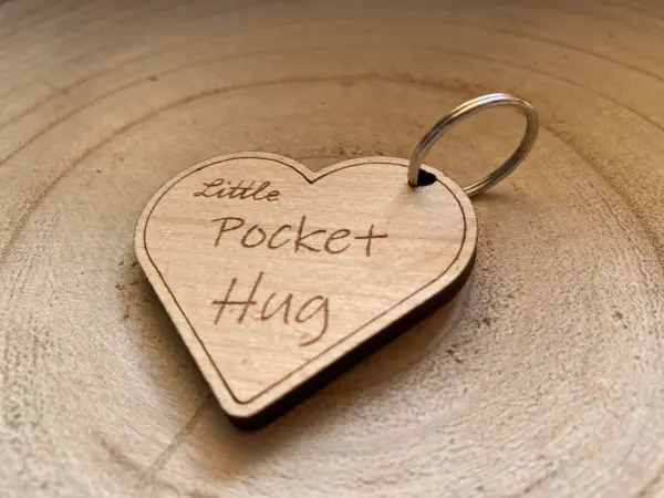 A personalized Little Pocket Hug Heart Shape Token Keyring rests on a light wooden surface—a thoughtful wooden keepsake for the First Day At School or Starting Nursery.