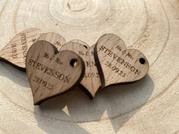 Four rustic heart-shaped wooden tags engraved with “Mr & Mrs STEVENSON” and “28.10.23” rest on a light wood surface—ideal as wedding favors or rustic wedding decor for your special day.