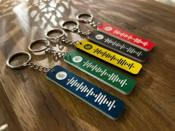 Five Personalised Song Spotify Code Keyrings in various colors with metal rings are displayed on a wooden surface. Each features a unique Spotify code—perfect gift for friends or family who love music.